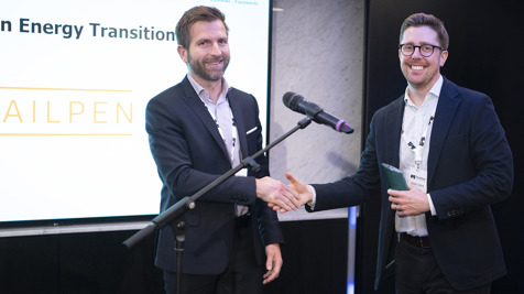 Two men in suits posing for a photograph in front of the screen. The screen features Railpen logo and says Energy Transition