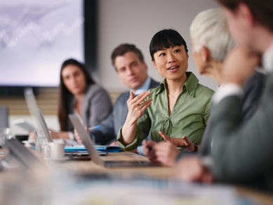 Woman speaks in row of people on laptops in a business meeting