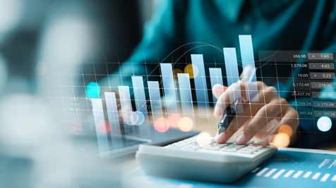 Hand holding a pen and using a calculator with sums visualised through graphs overlaid