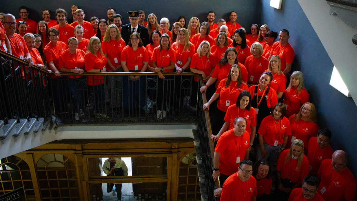 A large group of Railpen colleagues wearing matching red shirts gathered on the staircases and landing inside Stooperdale in Darlington, standing together in a historic rail‑heritage building.