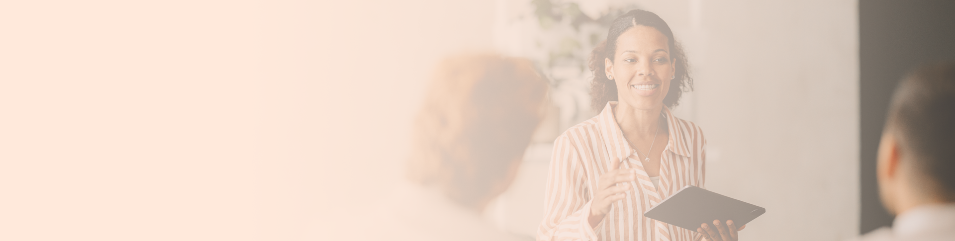 Two women and a man in an office setting. One woman faces the camera and holds a tablet. She talks to the other woman and the man.
