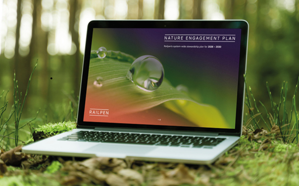 Laptop placed on the forest floor displaying Railpen’s Nature Engagement Plan cover, with a close‑up image of a water droplet on a leaf.