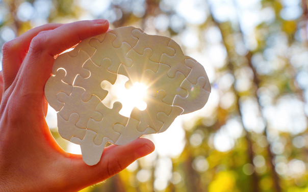 Hand holds jigsaw puzzle up to the sky with sunlight glowing through one missing piece