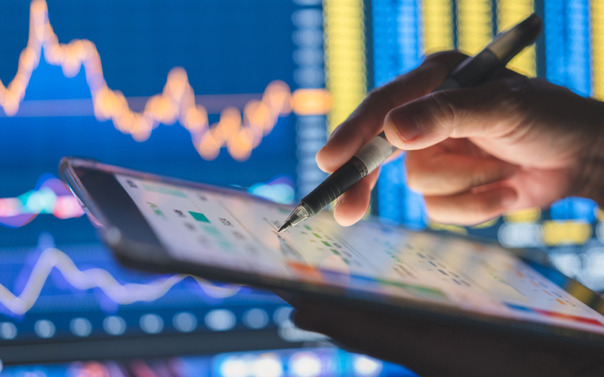 Digital pen hovers over tablet against a backdrop of investment graphics