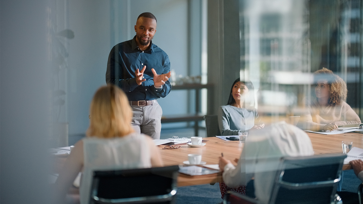 Man stands to present in a meeting of office workers