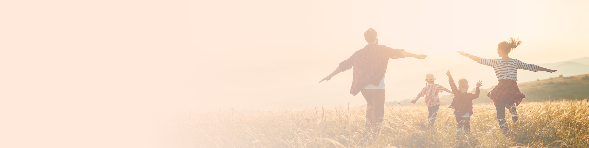 Two adults and two children at a field facing away from the camera. Their hands are spread suggesting they are happy.