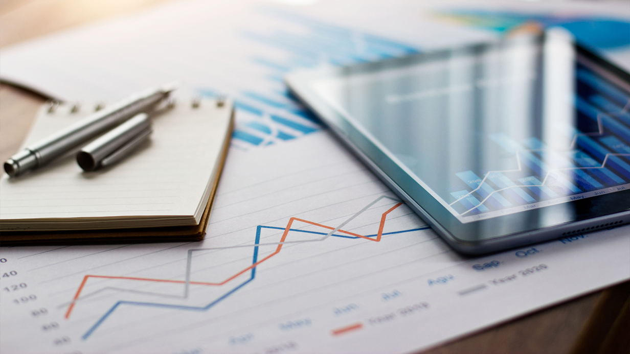 Desk covered in papers notepad and tablet showing reports and data