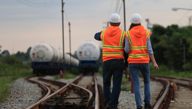 Two people in high vis jackets and hard hats standing at rail tracks