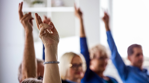 Several people sitting indoors with their hands raised, signaling participation or agreement during a group discussion.