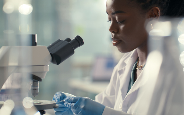 Woman in white lab coat and blue latex gloves places slides under microscope