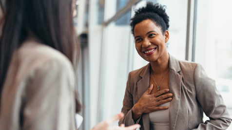 Two women talking in an office wearing beige business attire